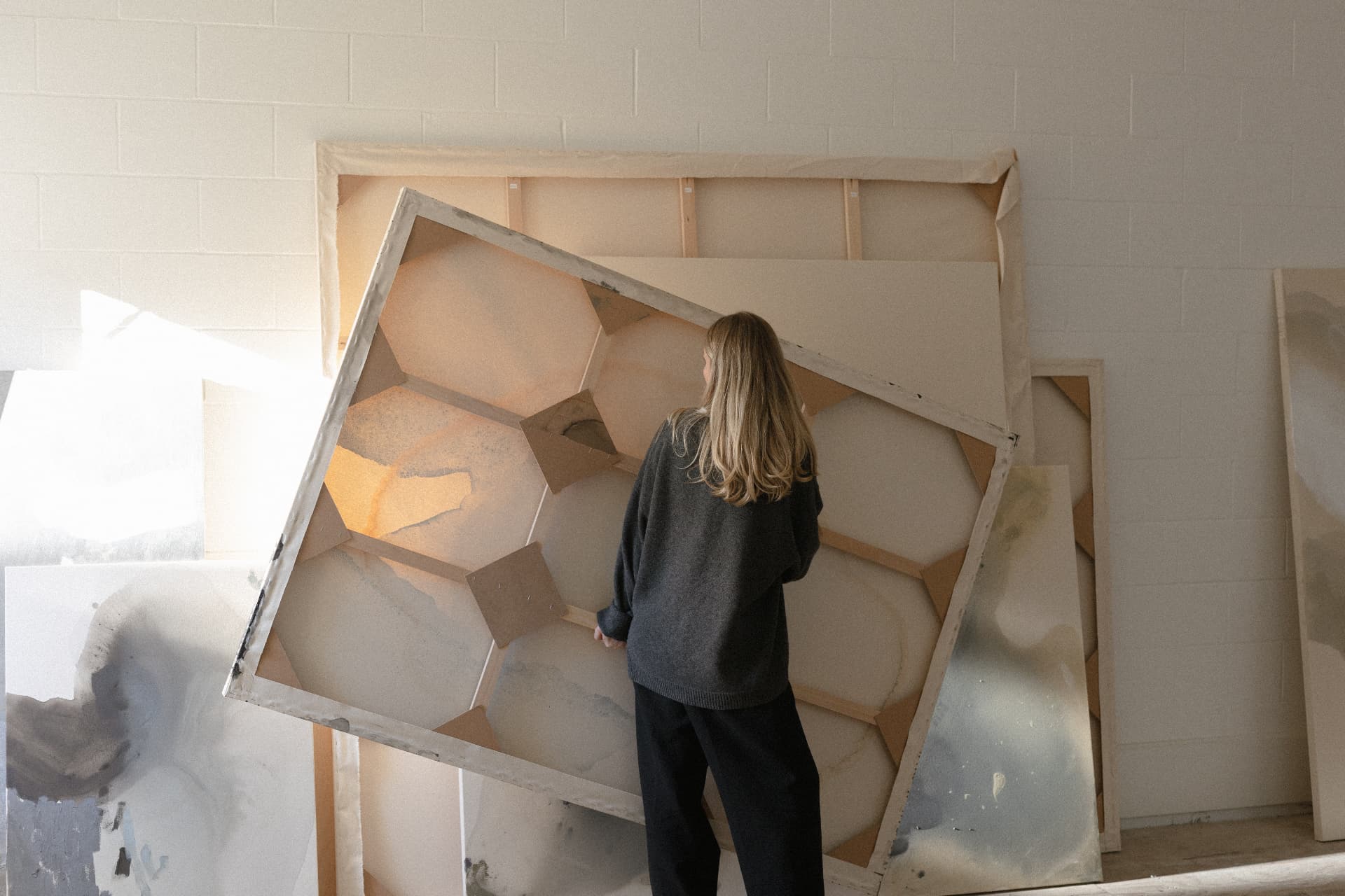 joy kinna leaning a large stretched canvas against others in her studio