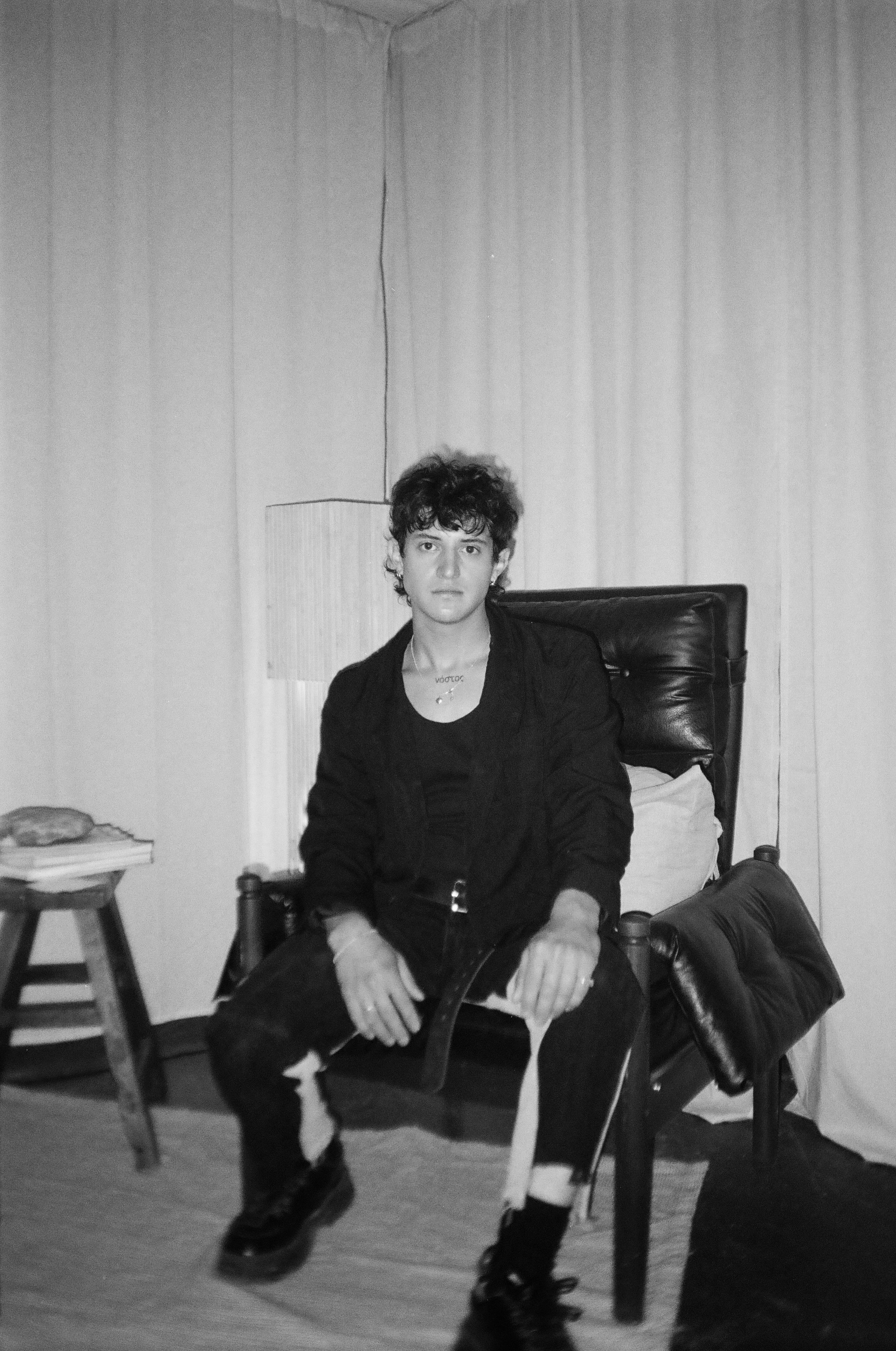a young person with curly hair sitting on a chair beside a side table of books
