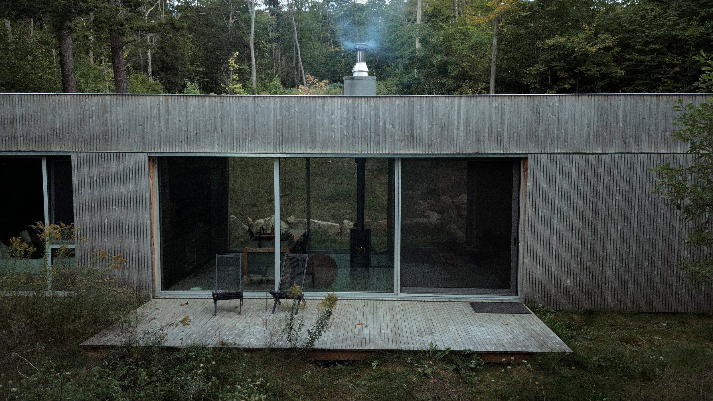 a timber cabin with floor-to-ceiling glass set among tall trees at dusk