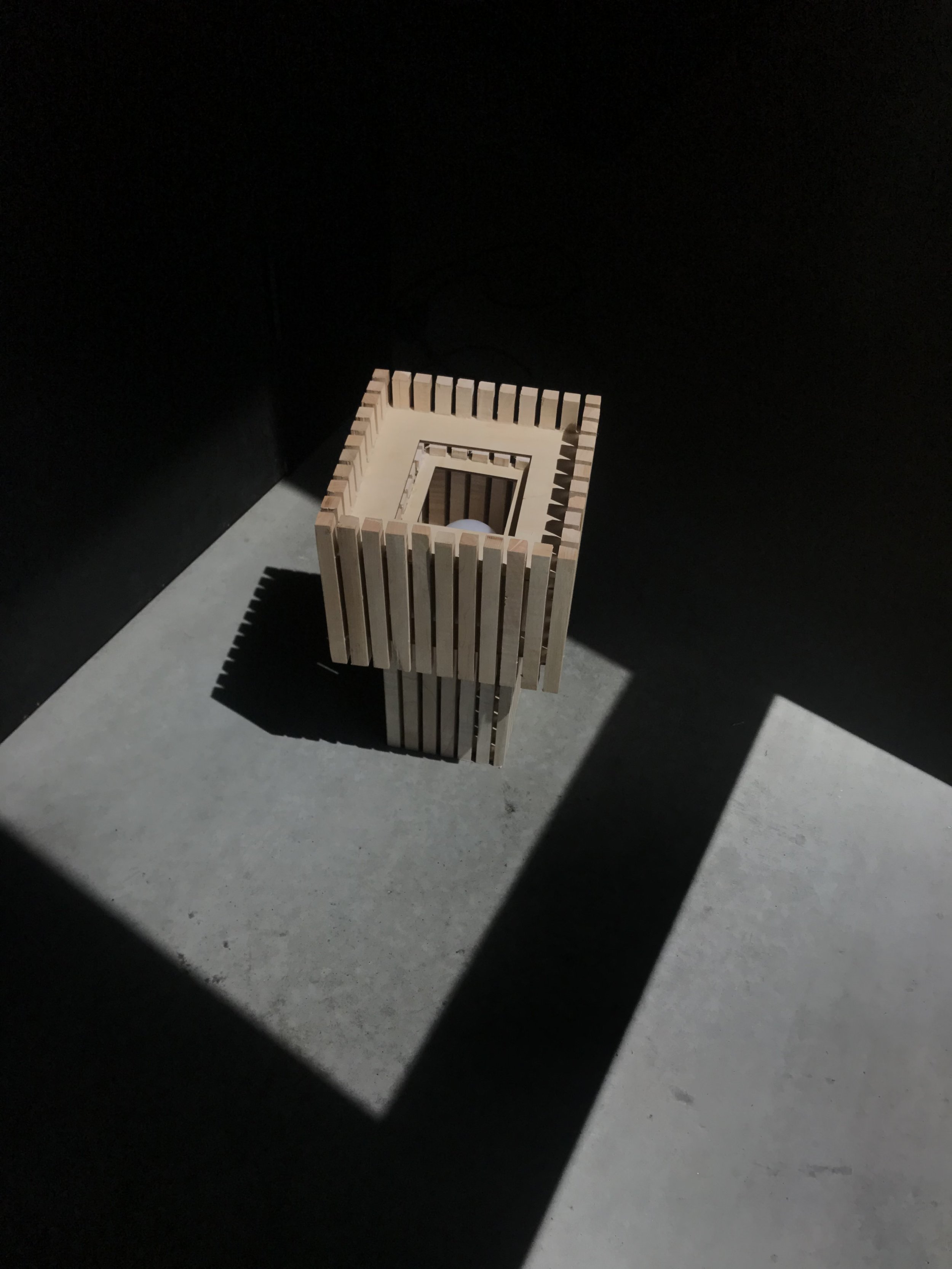 a rectangular wooden lamp made of evenly spaced vertical slats, casting shadows in a dark room